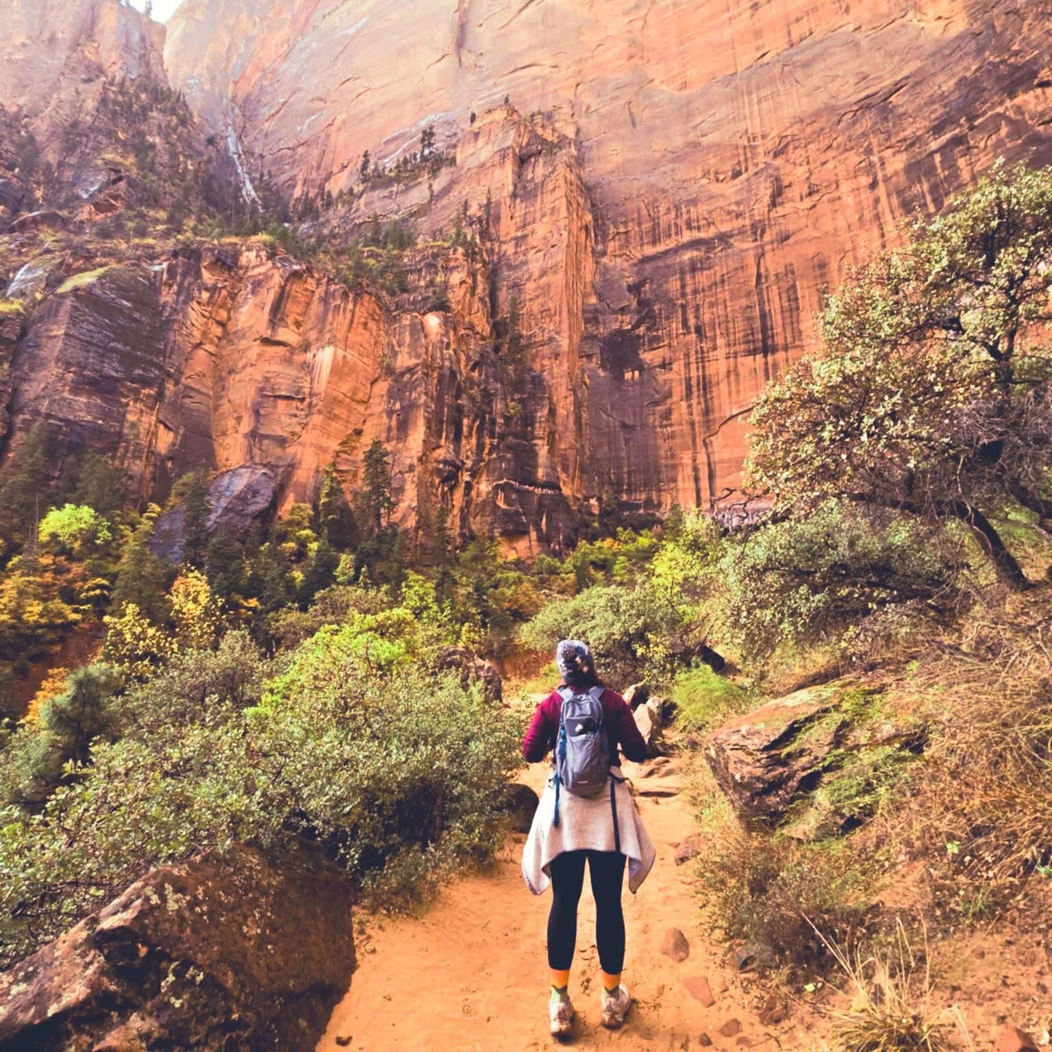 Brittany Lynn Armstrong hiking a sandy trail toward towering red canyon walls.